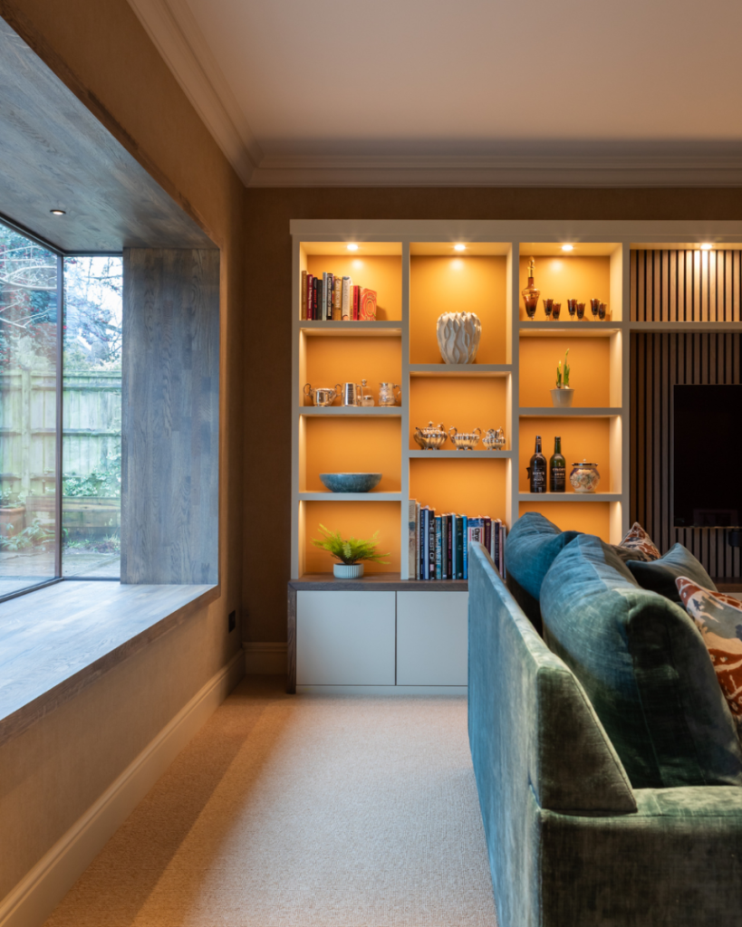 Contemporary living room with illuminated built-in shelving, modern sofa, warm neutral tones, and large picture window.