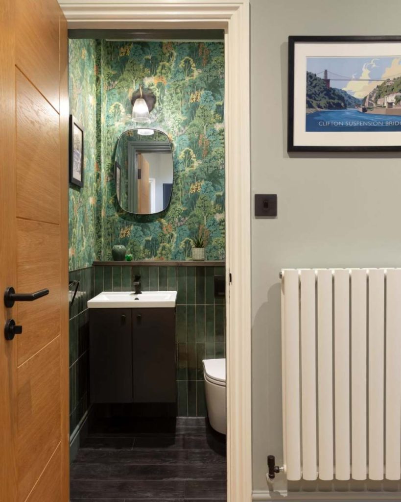 Contemporary bathroom in Guildford with botanical wallpaper, dark green tiles, modern vanity unit, matte black fixtures, and wooden door.