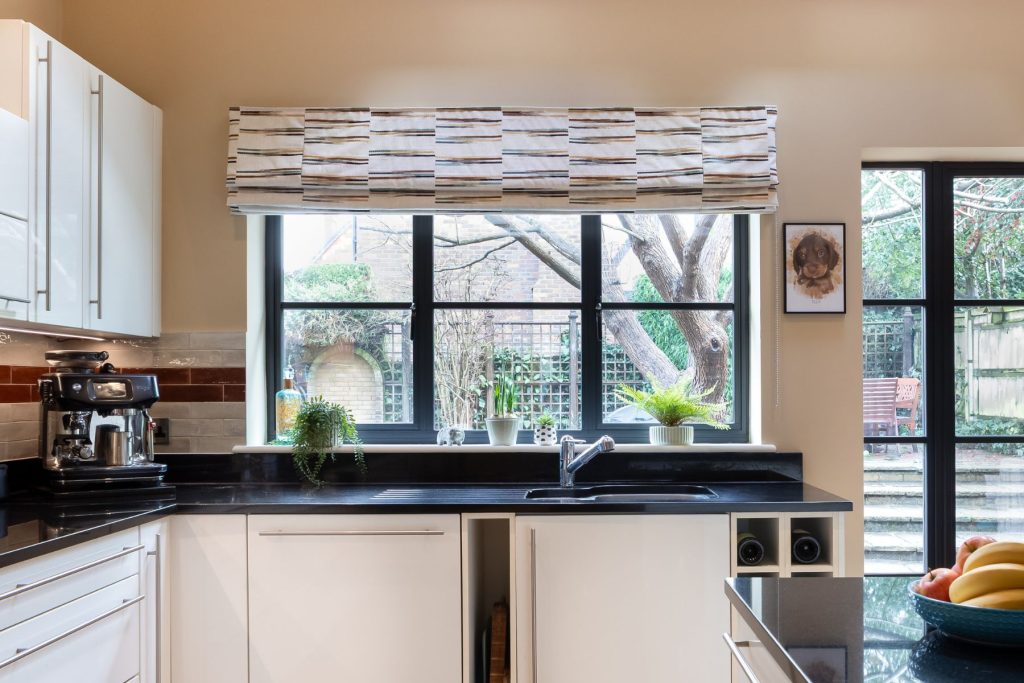 Contemporary kitchen with black worktops, white cabinetry, modern sink, and large window overlooking garden.