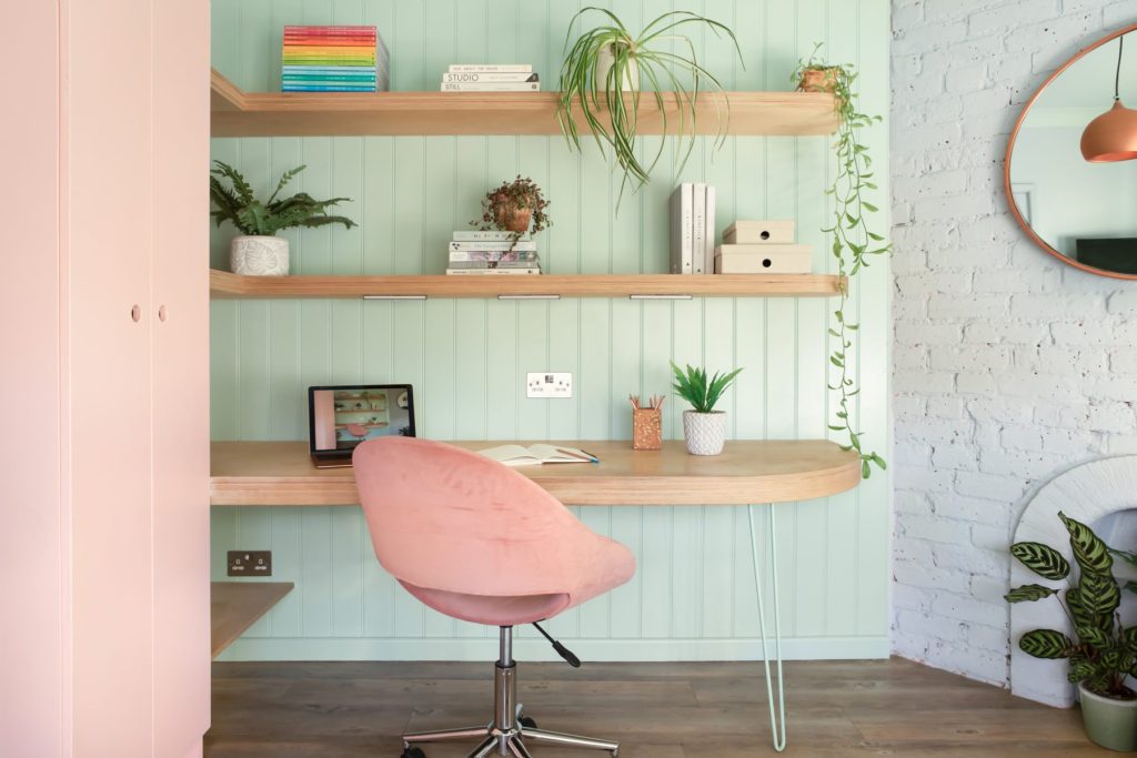Soft-toned built-in shelving with books, decorative objects, and modern desk lamp beside blush cabinetry.
