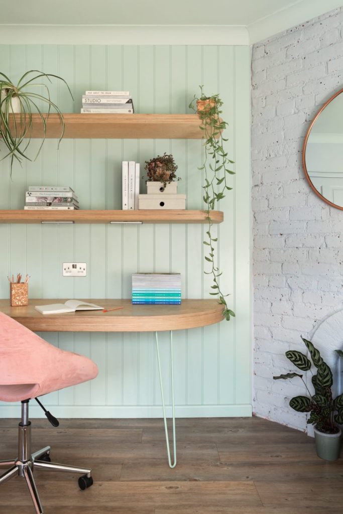 Soft-toned built-in shelving with books, decorative objects, and modern desk lamp beside blush cabinetry.