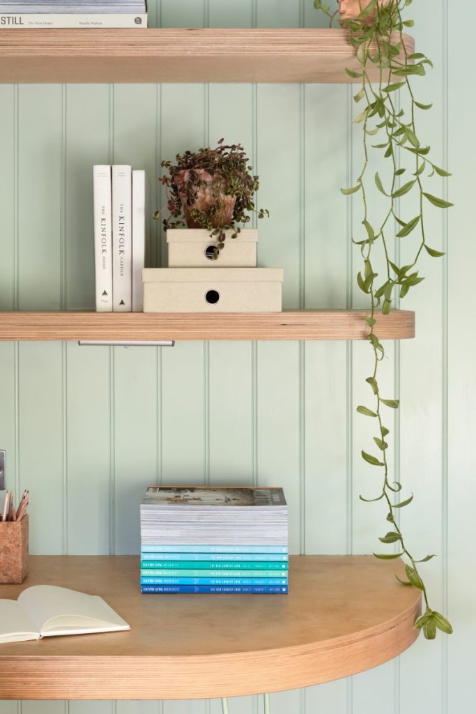 Soft-toned built-in shelving with books, decorative objects, and modern desk lamp beside blush cabinetry.