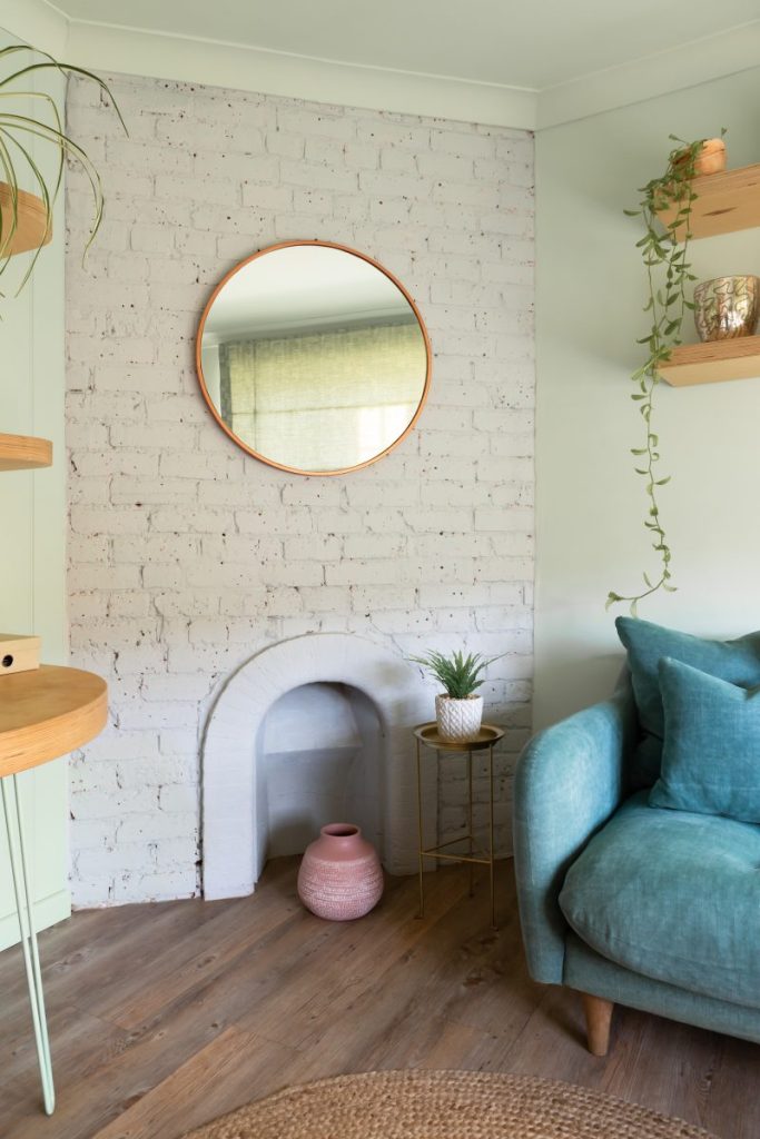 Styled lounge corner with decorative fireplace, round mirror, floating shelves and upholstered armchair.