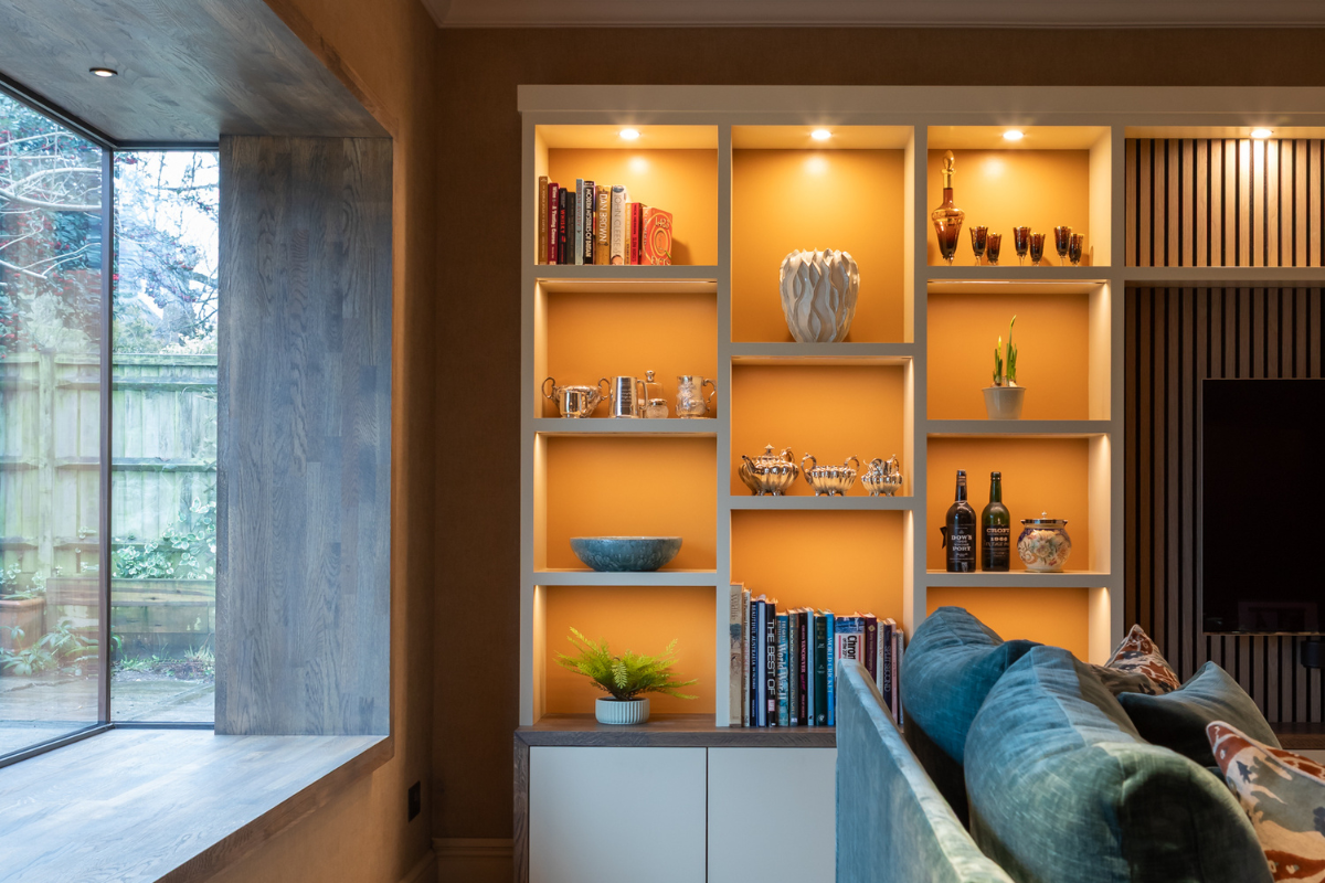 Contemporary living room with illuminated built-in shelving, modern sofa, warm neutral tones, and large picture window.