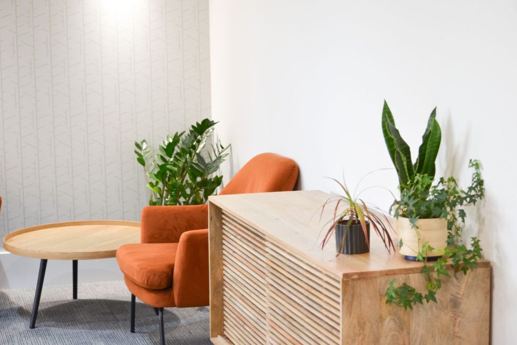 Office breakout seating with round wooden tables, orange chairs and indoor planting