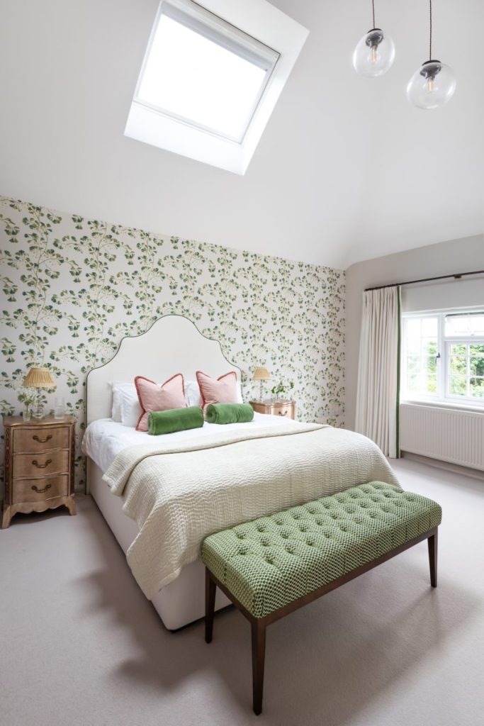 Bedroom with upholstered headboard, floral wallpaper, wooden bedside tables and layered cushions in soft pink and green tones.