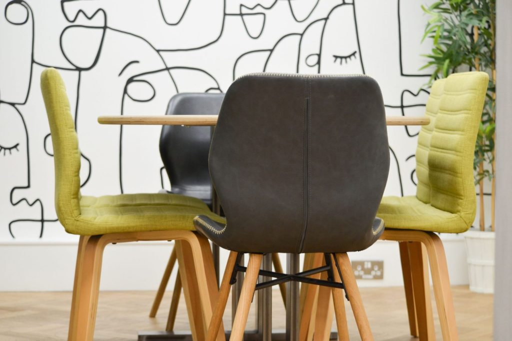 Modern office meeting area with wooden table, mixed seating, and graphic feature wall.