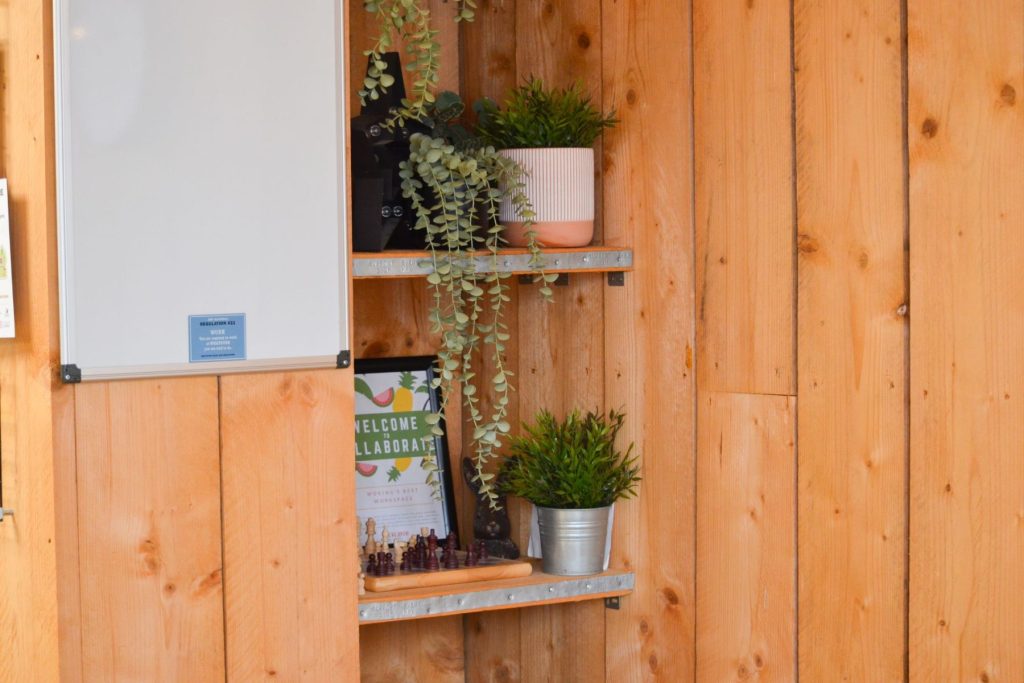 Modern office interior detail with wooden wall, floating shelves, indoor plants, and workspace styling.