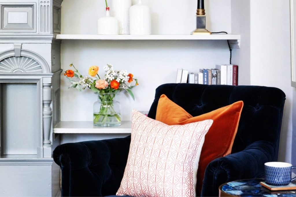Contemporary lounge area with velvet sofa, decorative cushions, bookshelves, and floral arrangement.