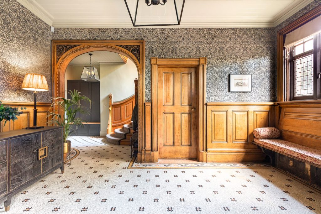 Period hallway featuring restored wooden panelling, decorative wallpaper, mosaic tiled flooring and an arched doorway leading to a staircase.