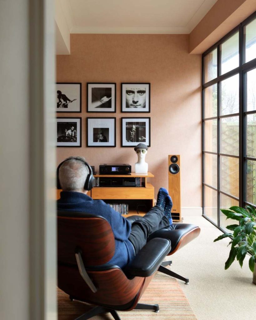 Modern listening room with lounge chair, high-end speakers, framed music artwork, and large industrial-style windows.