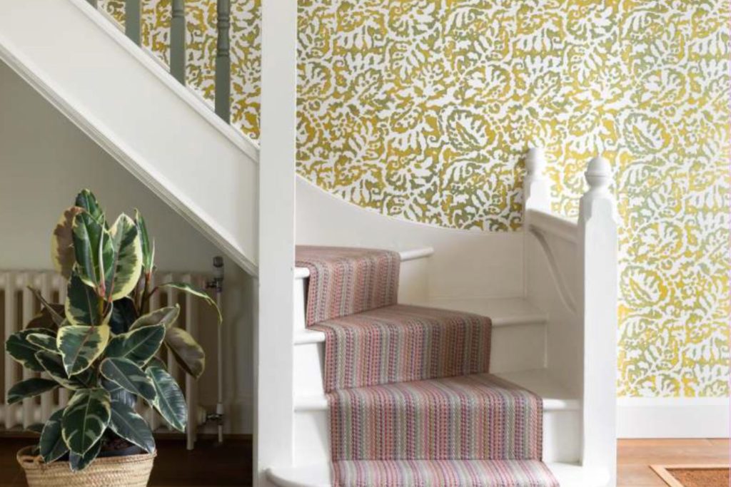 Contemporary staircase with patterned wallpaper, striped stair runner, white balustrade, and indoor plant.
