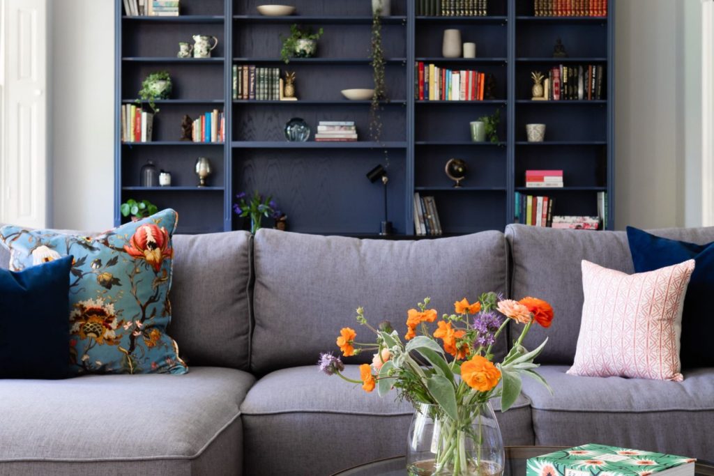 Elegant living room with bespoke blue shelving, statement chandelier and grey sectional sofa.