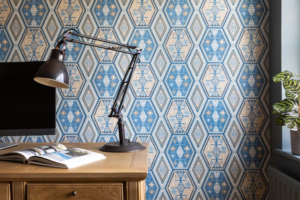 Contemporary home workspace with wooden desk, adjustable task lamp, patterned blue wallpaper, and modern styling.
