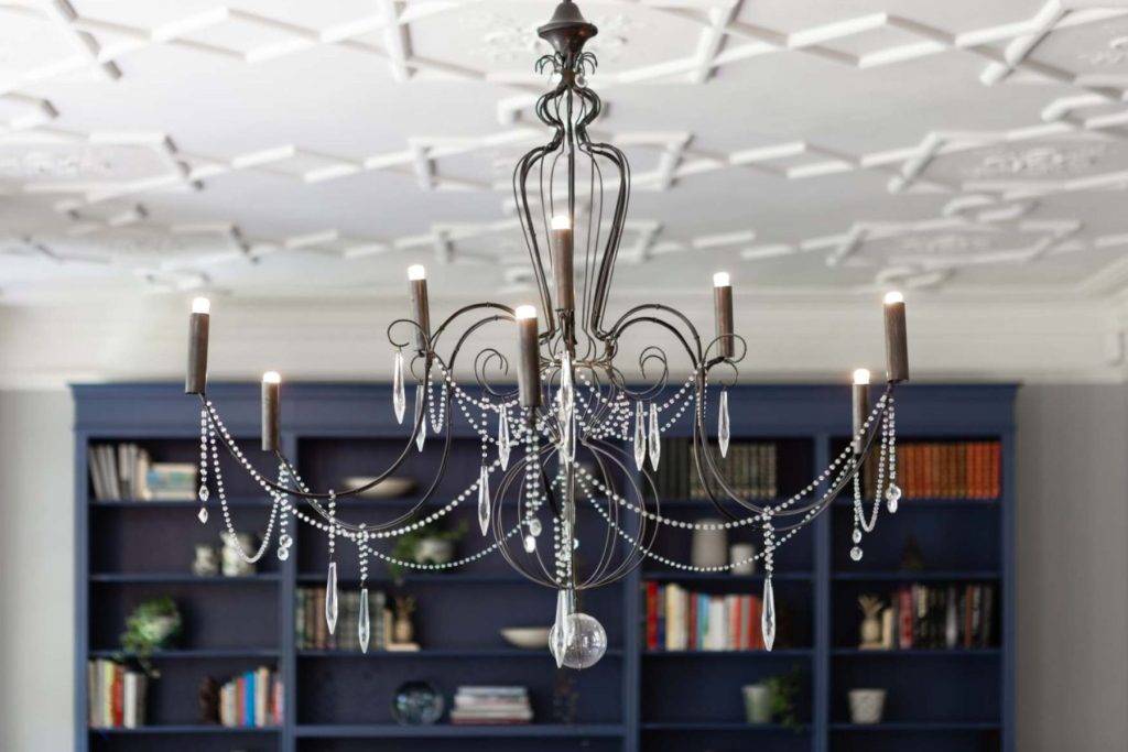 Decorative chandelier set against bespoke blue shelving and detailed ceiling.