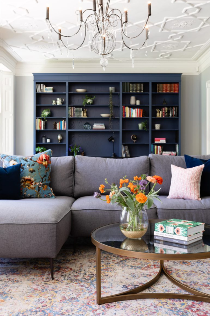 Contemporary lounge with bespoke blue shelving, grey sectional sofa, and brass coffee table.