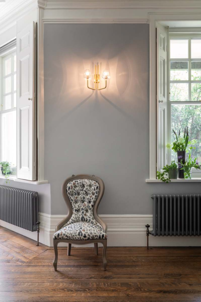 Contemporary seating vignette with upholstered accent chair, wall sconce lighting, and herringbone wood flooring.
