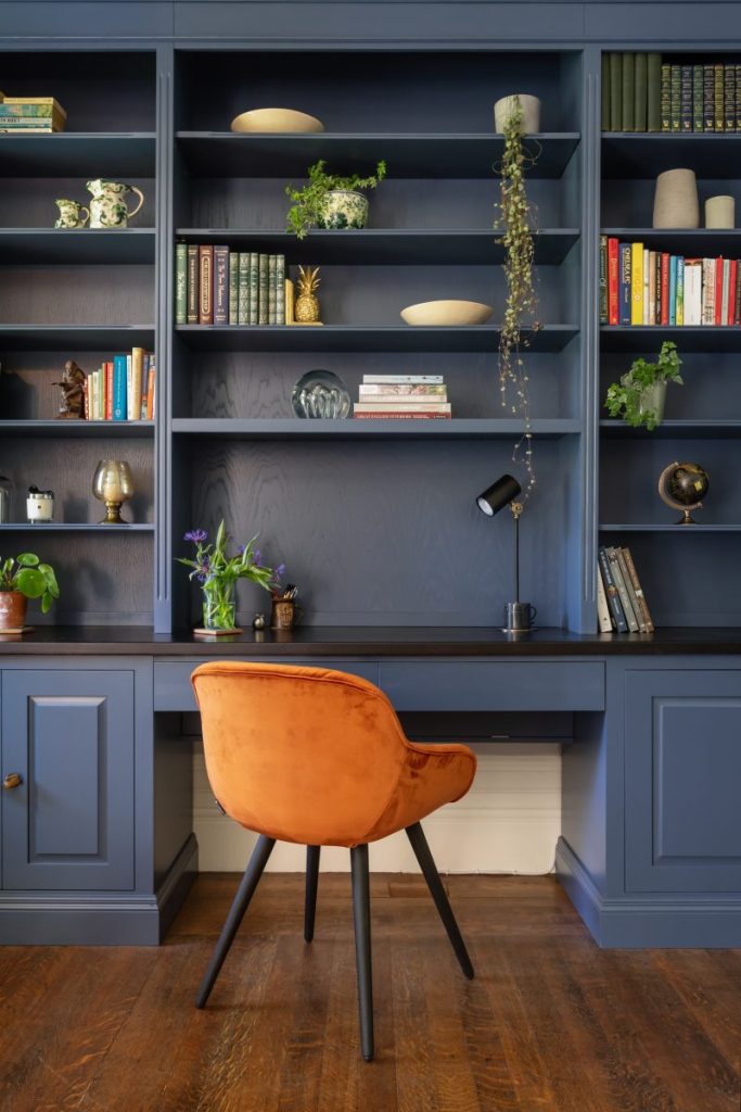 Contemporary workspace with bespoke blue shelving, styled bookcase, and rust velvet accent chair.